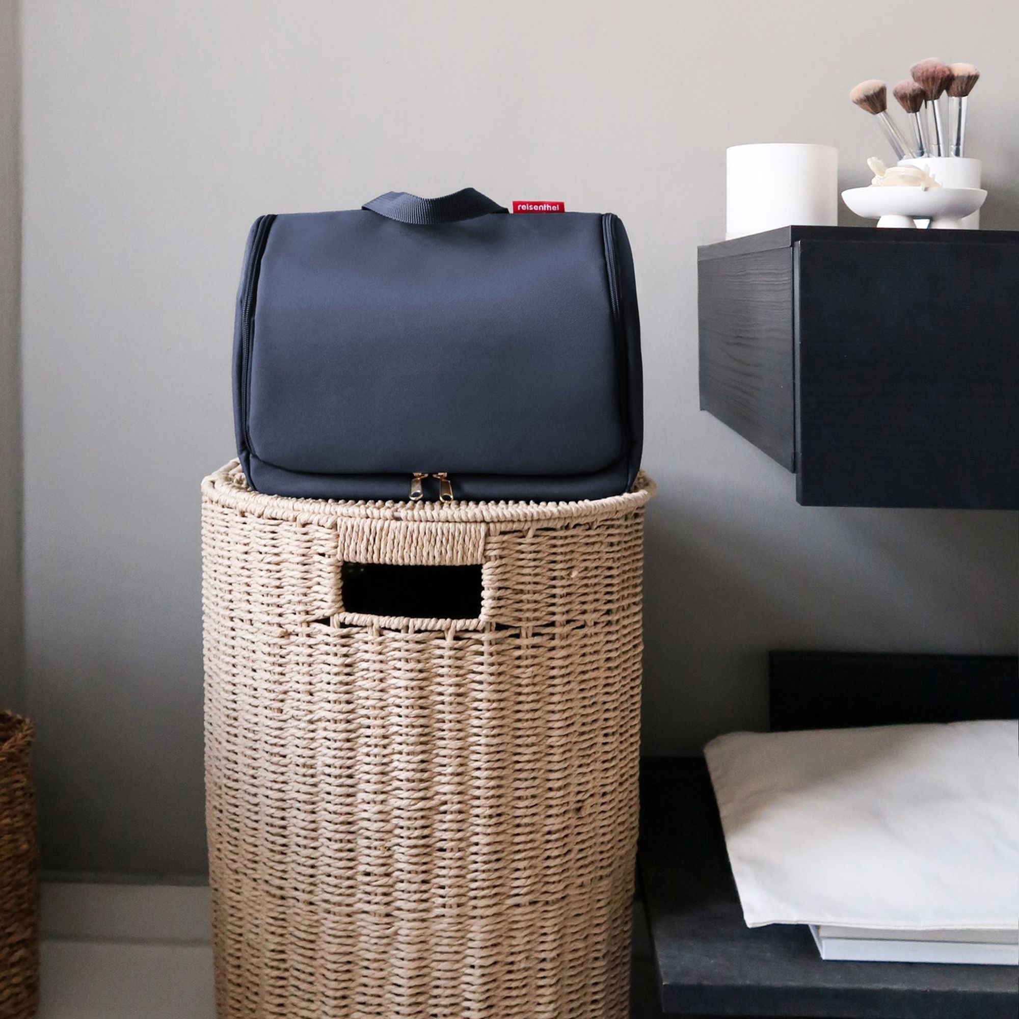 Dunkelblaue Kulturtasche auf geflochtenem Wäschekorb