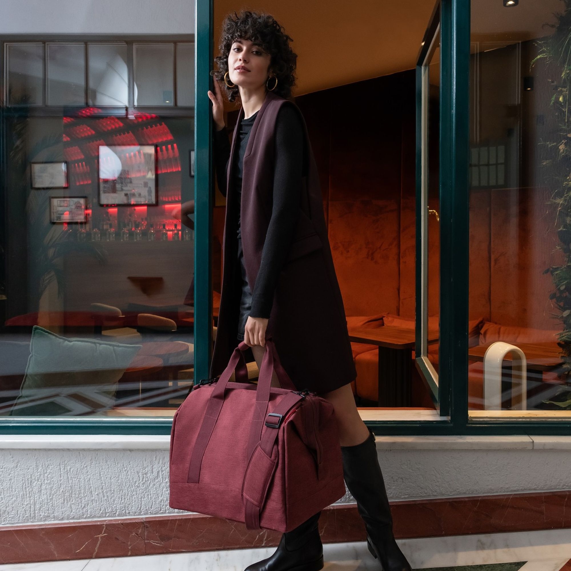 Frau mit burgunder Reisetasche vor stylischer Lounge
