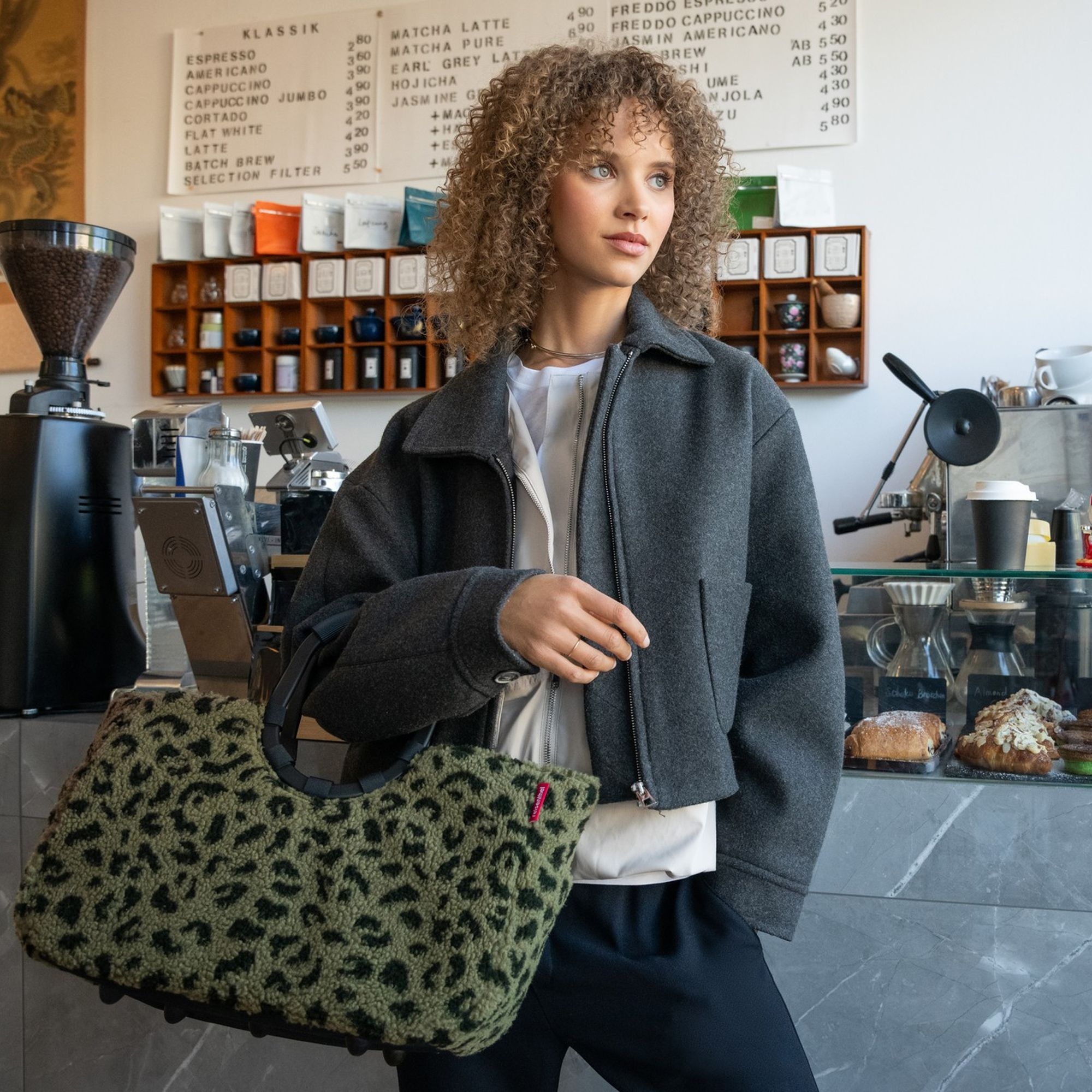 Frau mit grauer Jacke und grüner Leo-Tasche im Café